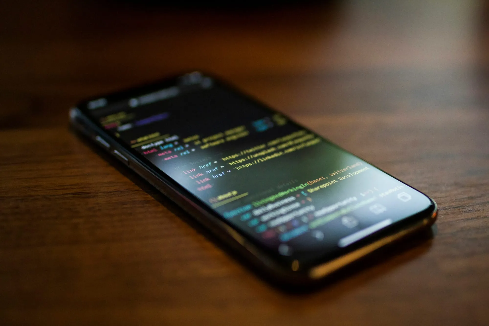 Smartphone on wooden table displaying colorful code or terminal text